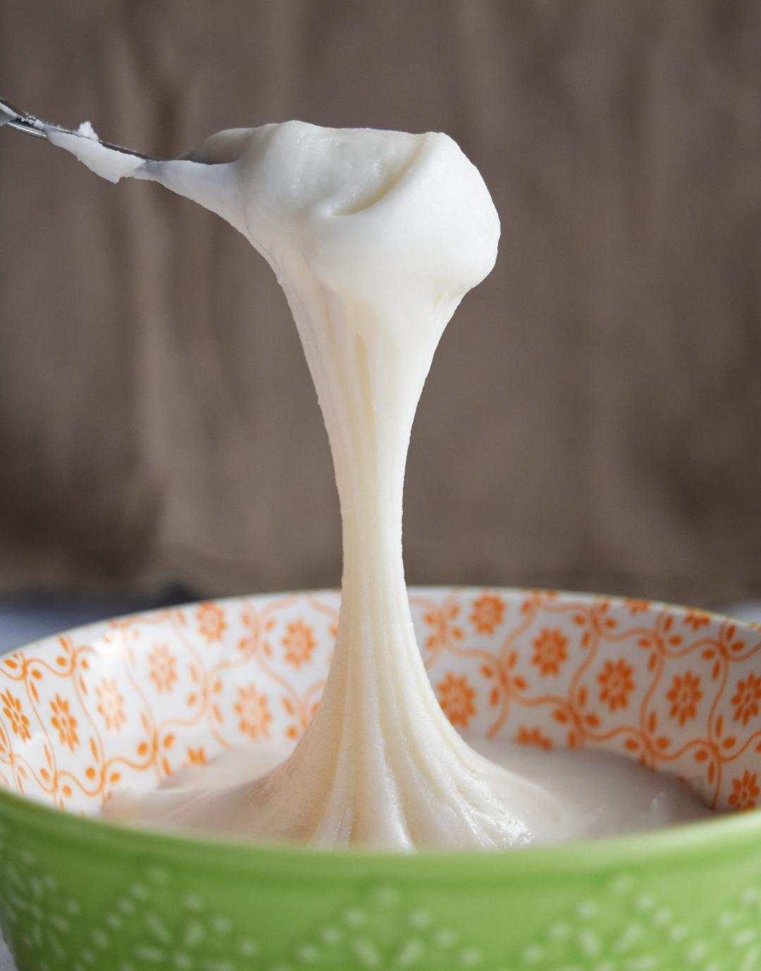 cream cheese frosting dripping from a spoon into a bowl